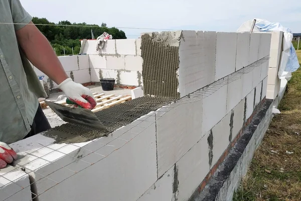 En byggnadsarbetare sätter ett block på murväggen och använder lim och hjälpverktyg. — Stockfoto