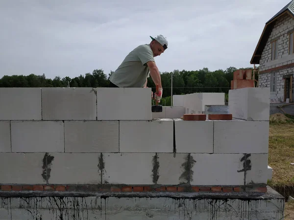 The master performs construction work, namely, laying a wall of gas blocks with tools and adhesive mortar, in the background the sky and the forest. — Stock Image The master performs construction work, namely, laying a wall of gas blocks with tools and adhesive mortar, in the background the sky and the forest. Stock Image
