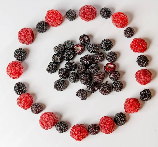 Red and black raspberries laid out in a circle on a white background.