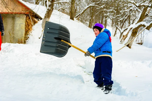 Depois de neve pesada, o menino limpa a neve com uma pá . — Fotografia de Stock