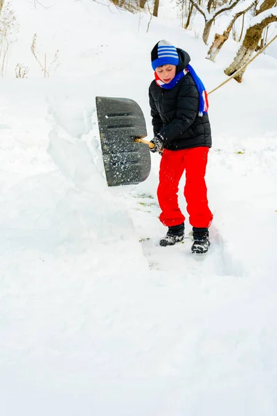 Depois de neve pesada, o menino limpa a neve com uma pá . — Fotografia de Stock