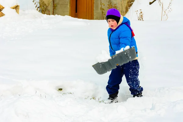 Menino com pá grande remove neve depois de uma tempestade de neve . — Fotografia de Stock