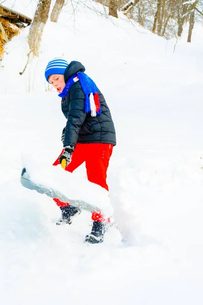 Pojken skyfflar snön nära sitt hus på vintern. — Stockfoto