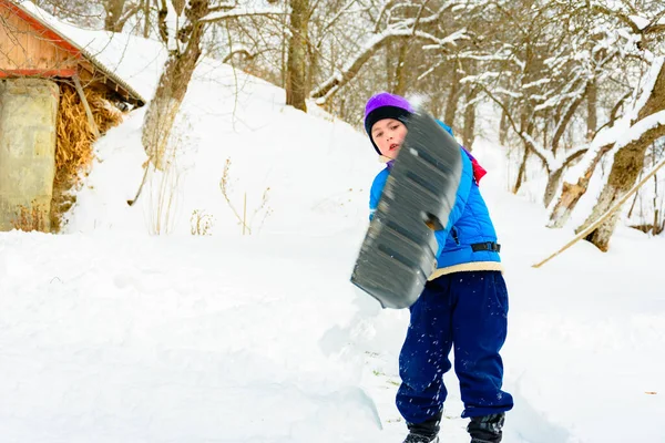 Nach starkem Schneefall räumt der kleine Junge den Schnee mit einer Schaufel. — Stockfoto