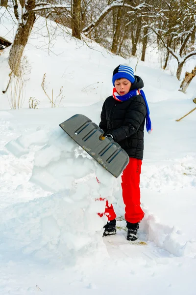 Der Junge schaufelt im Winter den Schnee in der Nähe seines Hauses. — Stockfoto