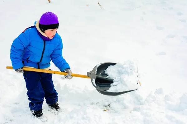 Rapaz sorridente está carregando neve em uma pá, criança limpa o quintal após uma queda de neve . — Fotografia de Stock