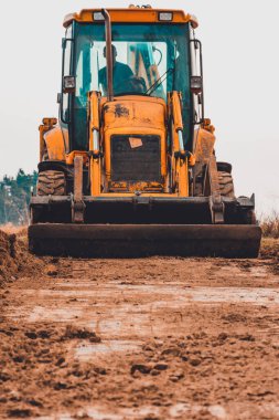 Kırsal kesimde bir kazıcı ön planda duruyor, büyük bir kova görünüyor..