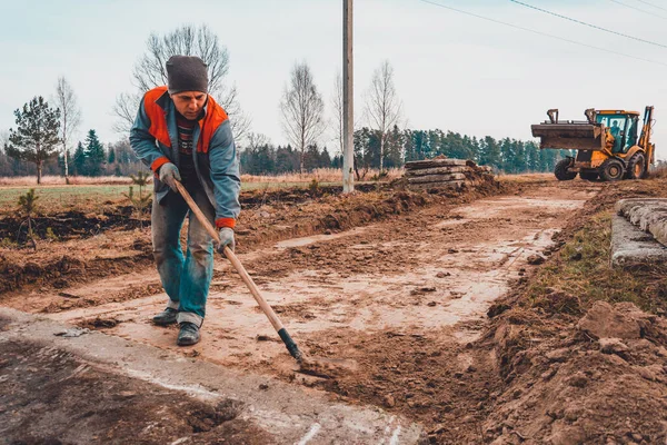 Екскаватор розчищає землю для дороги, працівник з лопатою допомагає у прокладанні дороги . — стокове фото