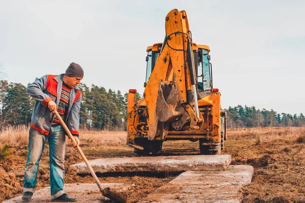O trabalhador da pá limpa o solo depois de cavar a escavadeira, colocando a estrada . — Fotografia de Stock