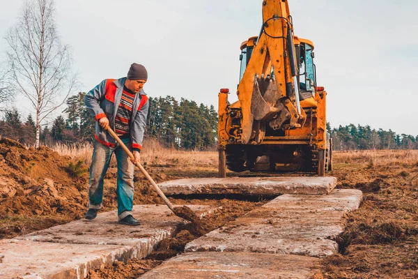 O trabalhador da pá limpa o solo depois de cavar a escavadeira, colocando a estrada . — Fotografia de Stock