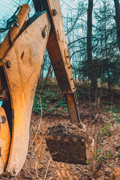 Una excavadora amarilla trabaja en el claro del bosque y cava tierra . —  Fotos de Stock