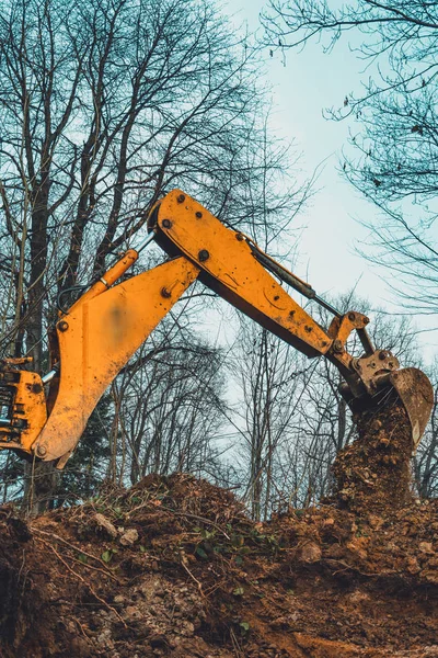 Ein gelber Bagger im Wald gräbt eine Grube für einen Teich. — Stockfoto