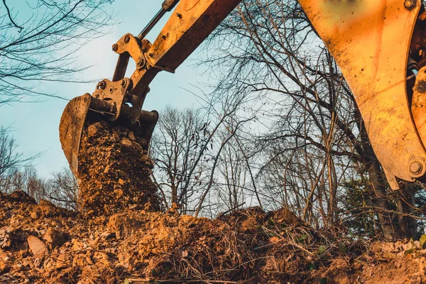Der Bagger führt Aushubarbeiten durch, indem er mit einer Schaufel im Wald den Boden aushebt. — Stockfoto