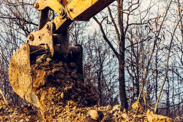 Der Bagger führt Aushubarbeiten durch, indem er mit einer Schaufel im Wald den Boden aushebt. — Stockfoto