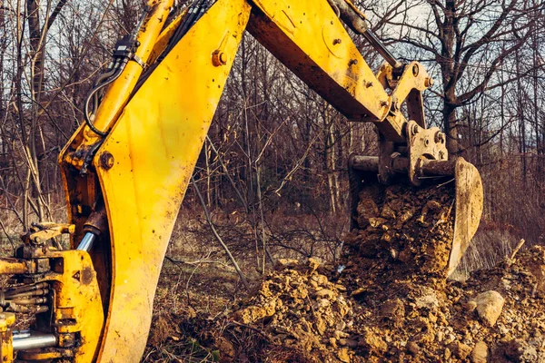 A escavadora realiza trabalhos de escavação escavando o solo com um balde na floresta . — Fotografia de Stock