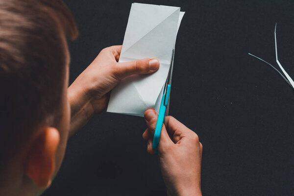 The boy of school age is engaged in application works, cuts white paper.