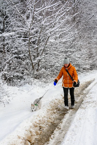 Piękna kobieta w pomarańczowej kurtce z husky szczeniaczkiem biegnącym przez leśną drogę. — Zdjęcie stockowe