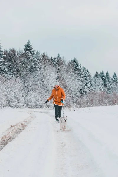 Hermosa mujer en chaqueta naranja con cachorro husky corriendo por el camino del bosque . —  Fotos de Stock