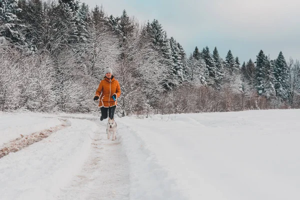 Ung kvinna löpare träning i Vinterparken med husky hunden — Stockfoto