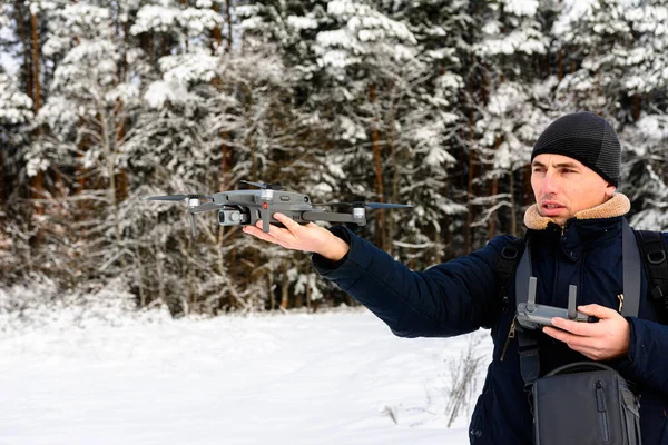 A young man launches a drone into the air in winter in the forest.