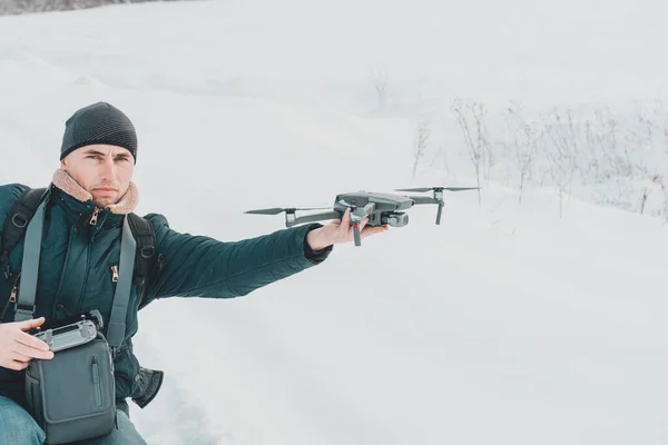 A young man launches a drone into the air in winter in the forest.