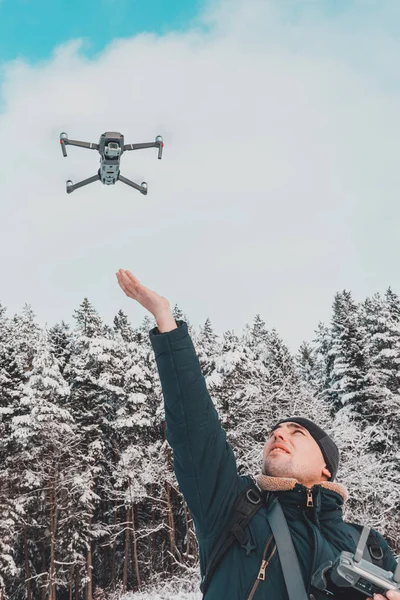 En man lanserar och tar bort en liten drönare eller quadcopter på en vit bakgrund av vinter och vinter skog. — Stockfoto