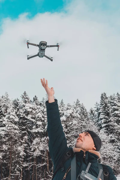 En man lanserar och tar bort en liten drönare eller quadcopter på en vit bakgrund av vinter och vinter skog. — Stockfoto