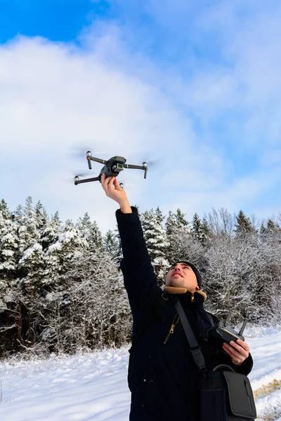 Bir adam kışın ve ormanın beyaz arka planında küçük bir dron veya kuadkopteri fırlatır ve kaldırır.. — Stok fotoğraf