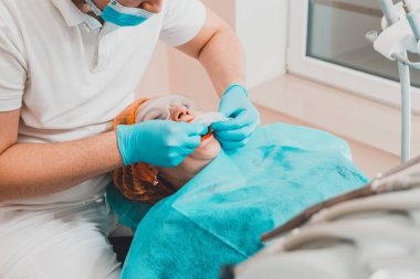 Genç bir dişçi diş kliniğinde ağız genişletme aleti çekiyor..