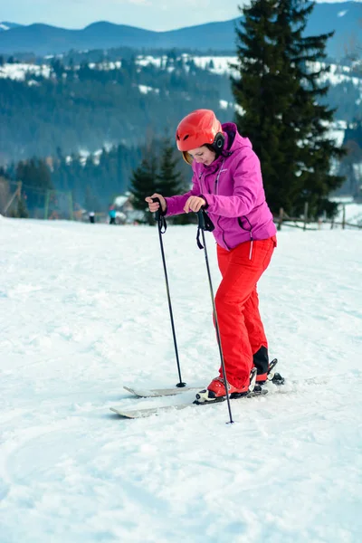 Foto de una joven deportista sonriente con casco de esquí en la mano contra el cielo azul y la colina nevada y pintorescos Cárpatos . — Foto de Stock