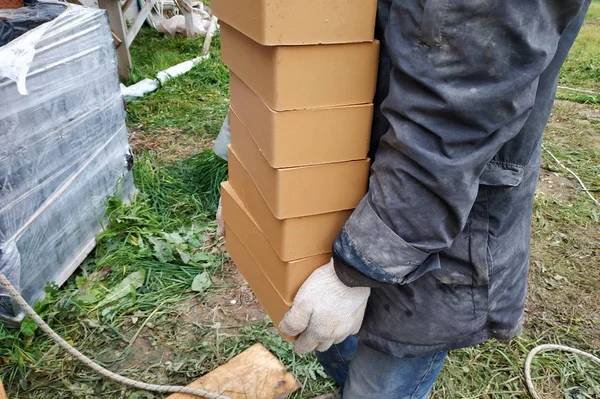 Montones de ladrillos anaranjados, apilados en filas, el trabajador lleva varias piezas . — Foto de Stock