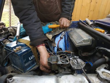 Adjustment of the motors' valves on a by an auto locksmith in a garage, dirty hands.