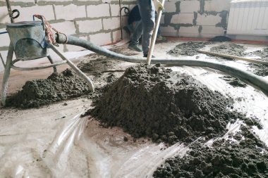 The worker performs a sand-cement floor screed above the floor heating.