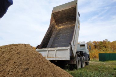 A dump truck unloads sand at a construction site to mix cement.