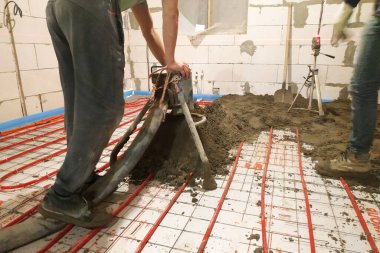 In the newly built house the worker performs a sand-cement screed for heating. clipart