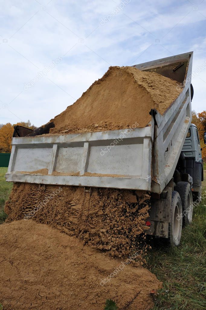 A dump truck unloads sand in the construction site.