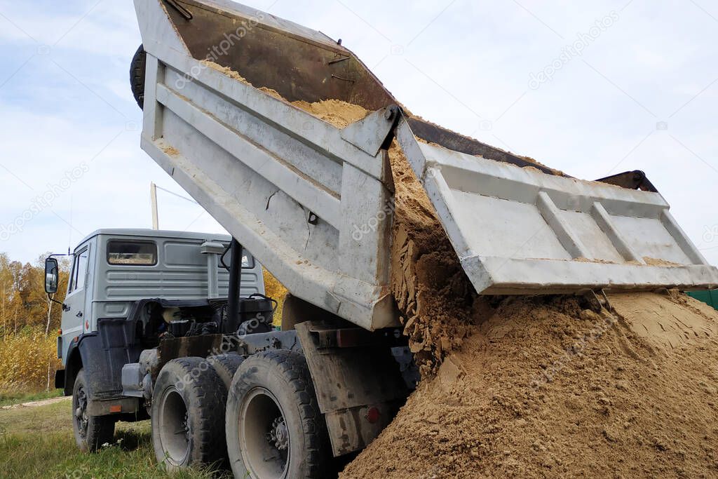 A dump truck unloads sand at a construction site to mix cement.