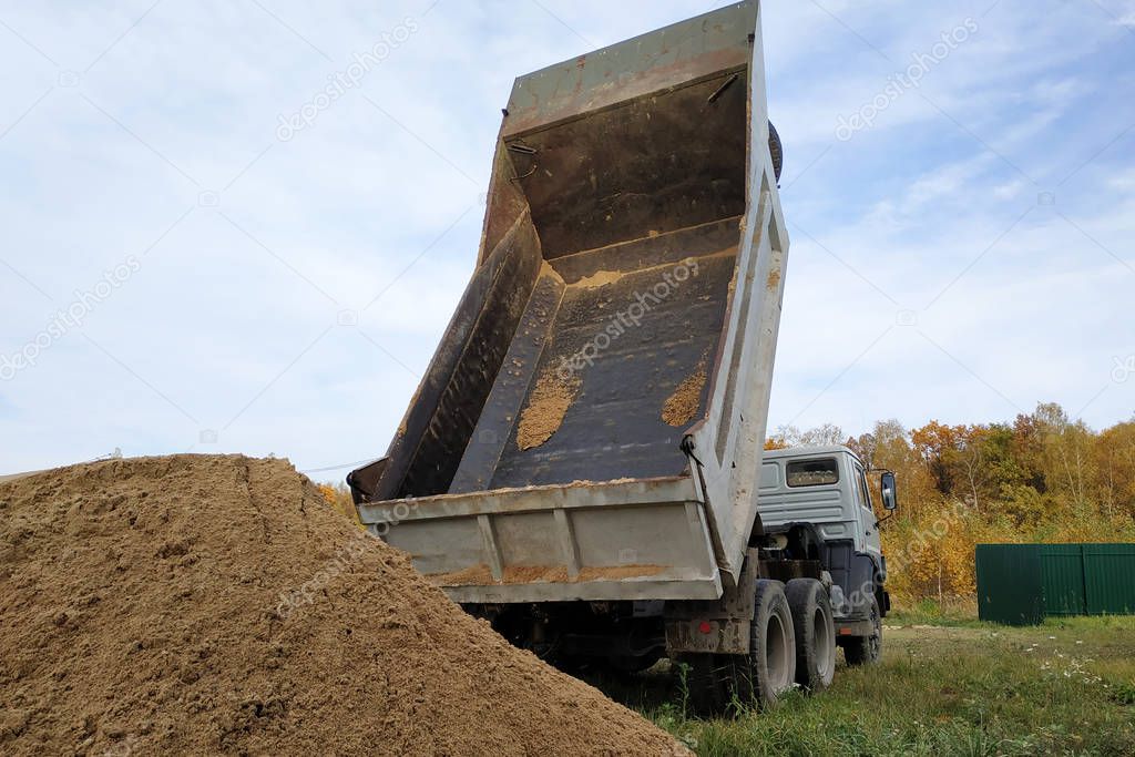 A dump truck unloads sand at a construction site to mix cement.