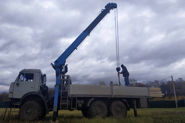 Crane on sky background unloads boards at construction site.