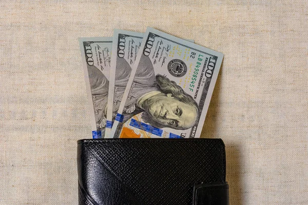 One hundred dollars lie in a black purse on a gray background. — Stock fotografie