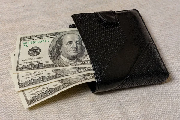 One hundred dollars lie in a black purse on a gray background. — Stock fotografie