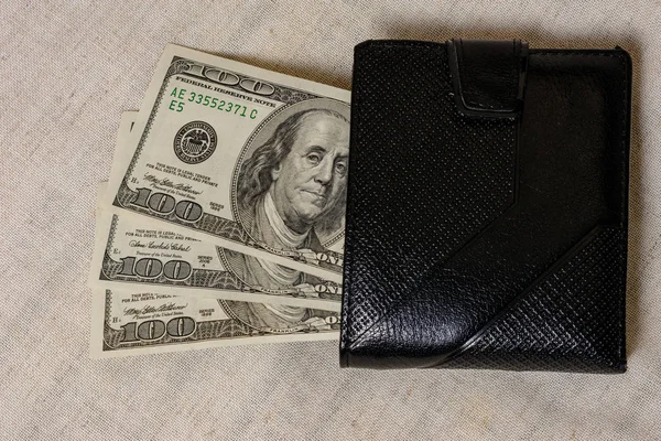 One hundred dollars lie in a black purse on a gray background. — Stock fotografie