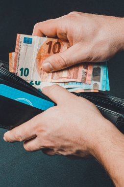 Man hand pulling money from wallet, black background and black wallet.