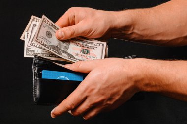 black wallet with dollars in man hands on black background.