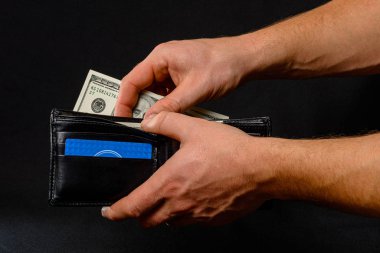 black wallet with dollars in man hands on black background.