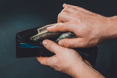 man removing dollars from his wallet, hands and wallet on black background.