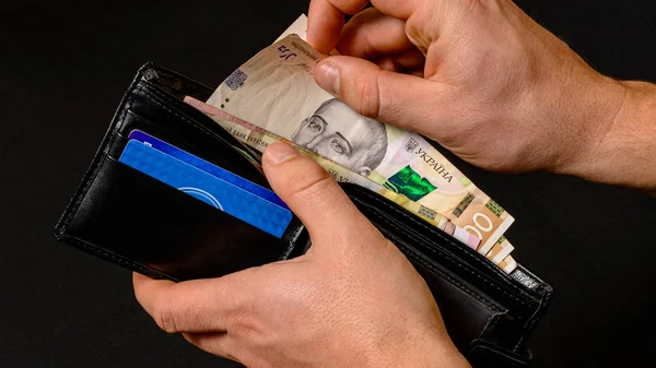 Closeup in the hands of a man's wallet when he pulls out a 500 hryvnia banknote.