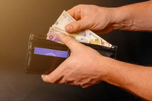Ukrainian hryvnia in a black purse, a man holds in his hands. — Stock Fotó