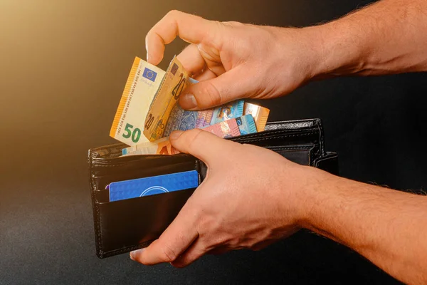 Closeup of human hands putting euro banknotes in wallet isolated on black background. — Stock Fotó