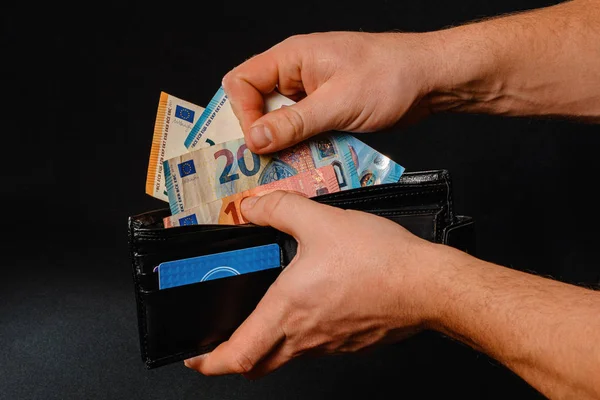 Closeup of human hands putting euro banknotes in wallet isolated on black background. — Stock Fotó